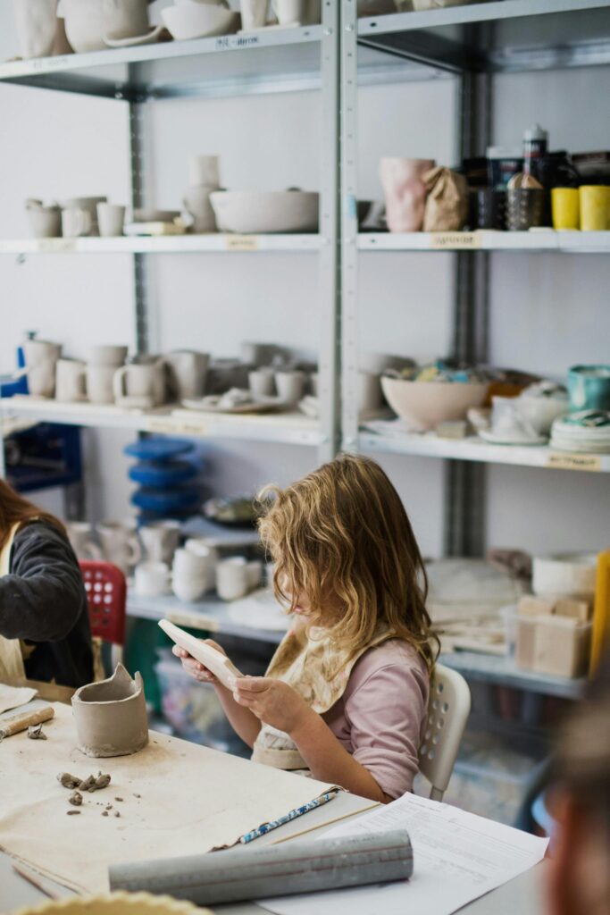 Young girl focused on crafting clay in a vibrant pottery workshop setting.