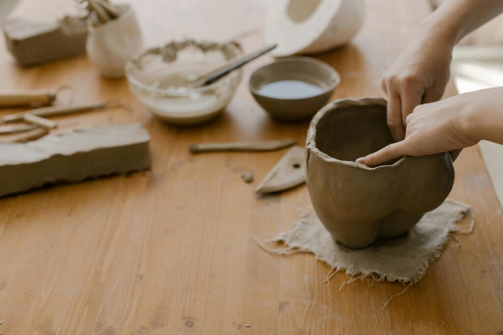 Close-up of hands molding clay into a pot, showcasing artistry and craftsmanship on a wooden tabletop.